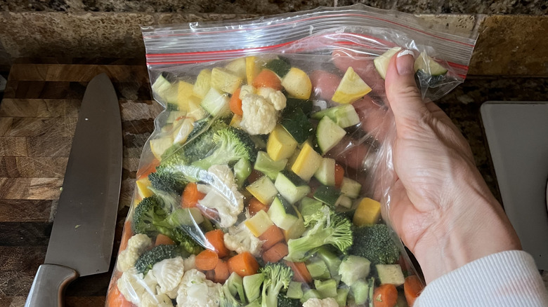 A hand places a plastic bag of vegetables on a countertop