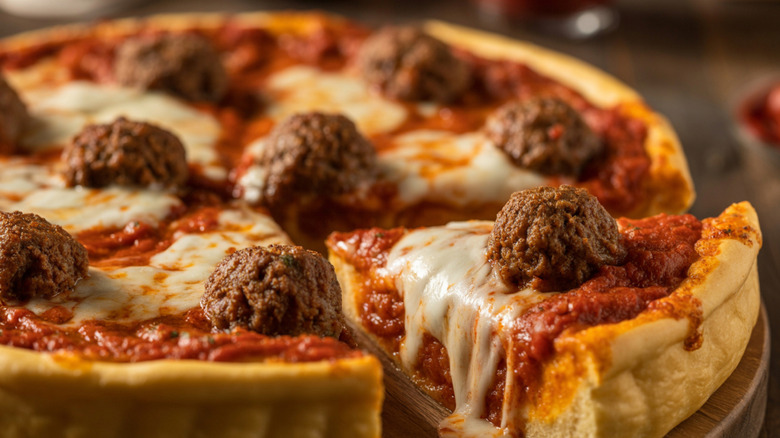 a thick, pan crust-style pizza with meatballs on top, one slice cut and offset from the pie