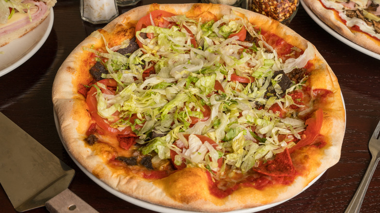 a taco pizza with beef, tomatoes, and lettuce on top