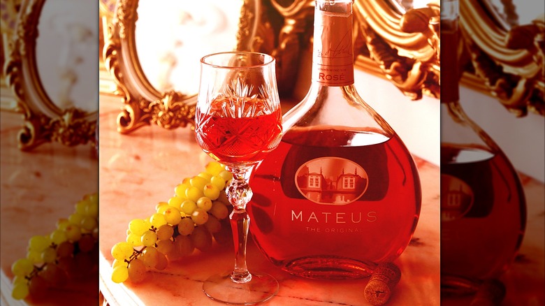 Glass of Mateus rose wine in front of bottle and bunch of grapes
