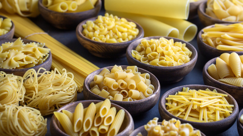 Various shapes of dry pasta in separate bowls on a table