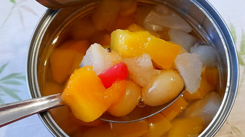 A metal spoon scooping fruit out of a can of fruit cocktail.