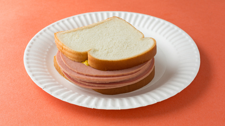 A bologna sandwich on white bread on a large paper plate.