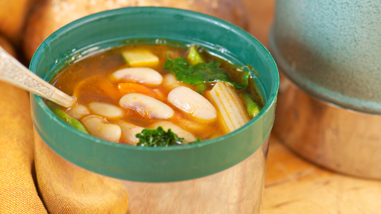 Minestrone soup inside a metal and green thermos with a spoon in it.
