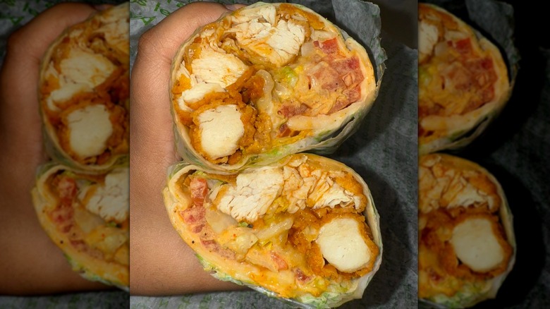 Hand holds a wrap with fried chicken cut in half