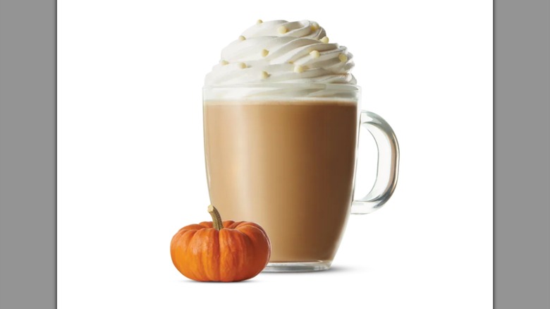 A tiny pumpkin in front of a mocha with whipped cream