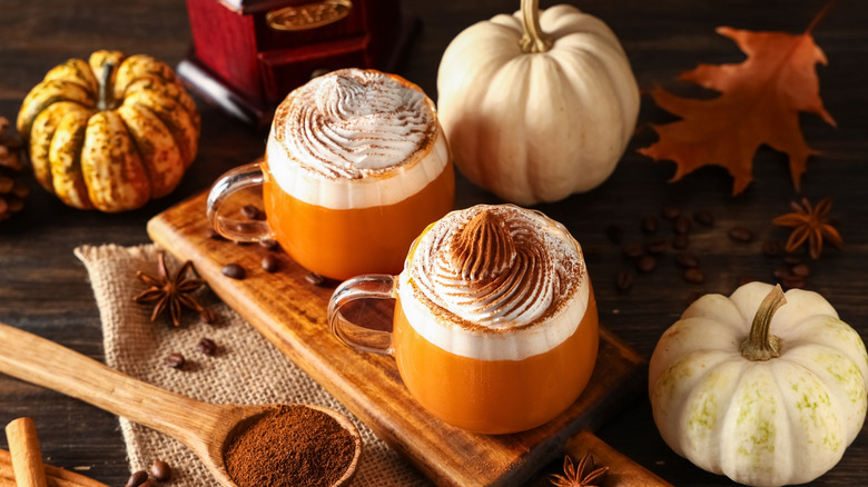 Several pumpkins next to two pumpkin spice lattes