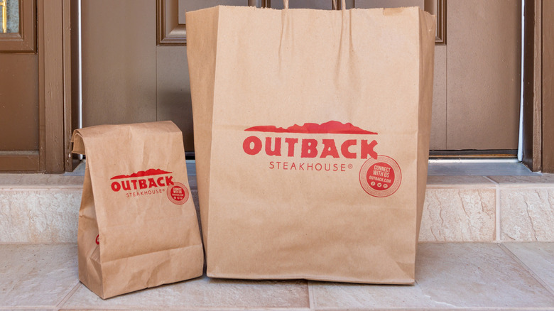 Two Outback Steakhouse bags sit in front of a door for takeout