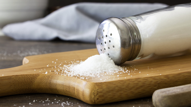 A salt shaker spilled over onto a wooden cutting board