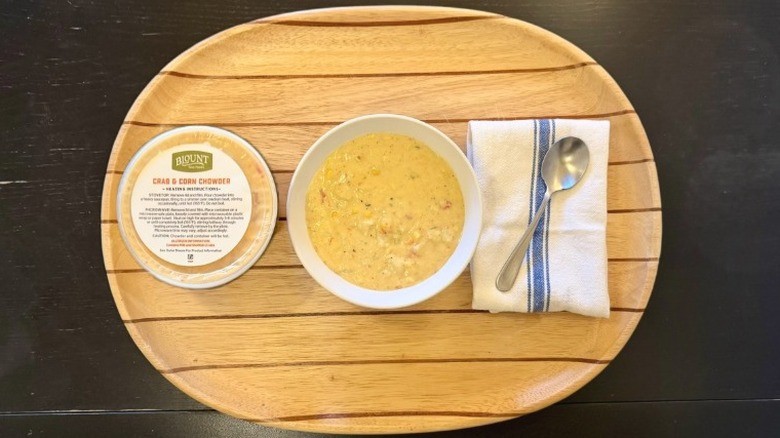 Blount Crab & Corn Chowder in a bowl on a wooden tray next to its container, a napkin, and a spoon