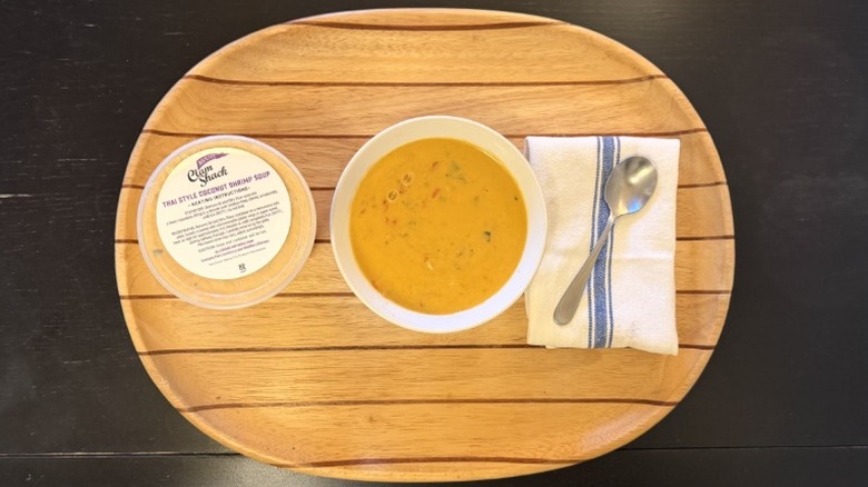 Blount Thai Style Coconut Shrimp Soup in a bowl on a wooden tray next to its container, a napkin, and a spoon