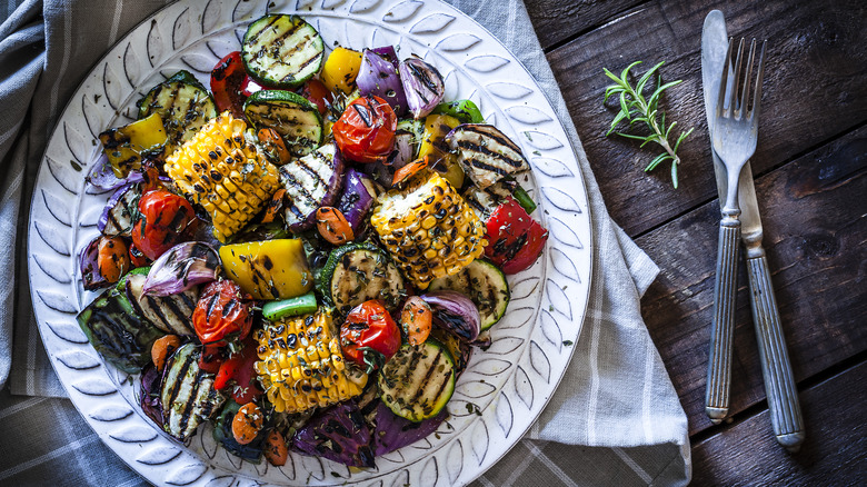 A plate of grilled mixed vegetables including corn, tomatoes, zucchini, and onions