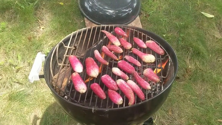 Several long, sliced radishes cooking face-down on a round charcoal grill