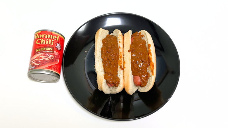 A can of Hormel Chili No Beans next to a black plate with two chili hot dogs