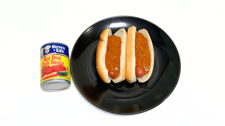 A can of Steve's and Ed's Hot Dog Chili Sauce with Jalapeño next to a black plate with two chili hot dogs