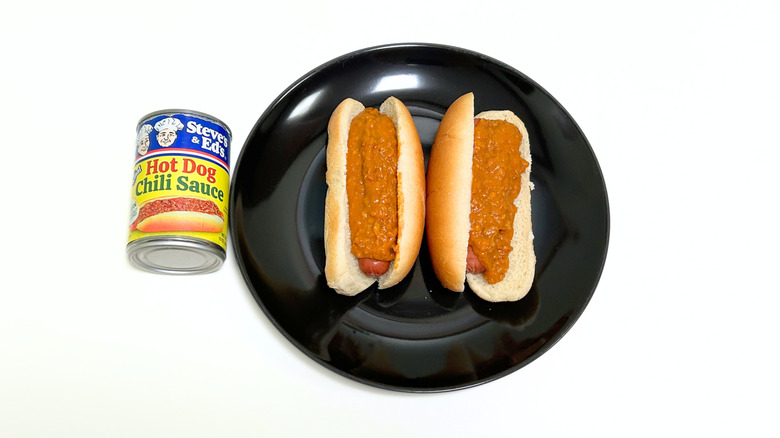 A can of Steve and Ed's Hot Dog Chili Sauce with Onion next to a black plate with two chili hot dogs