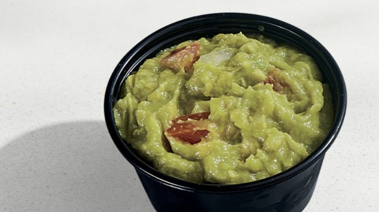 Taco Bell guacamole in a black takeout container on a white table