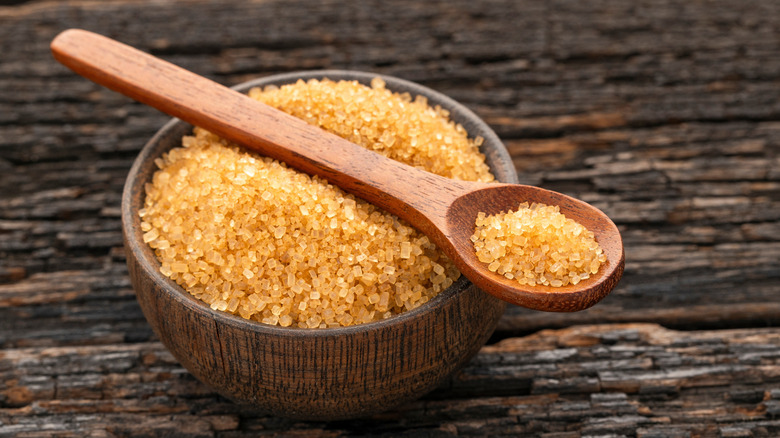 A wooden bowl full of raw sugar on a table with a wooden spoon balancing on top