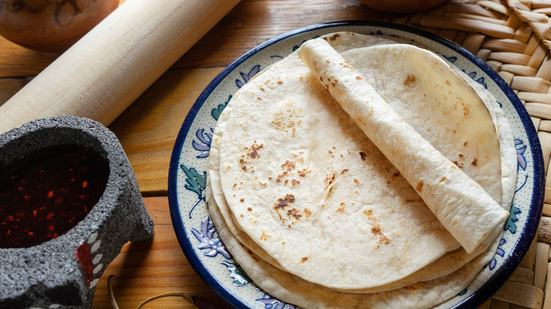 Flour tortillas on a white and blue decorative plate next to a cup of salsa