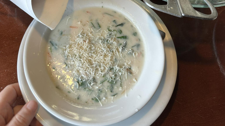 Overhead view of a hand reaching for a bowl of creamy Olive Garden soup