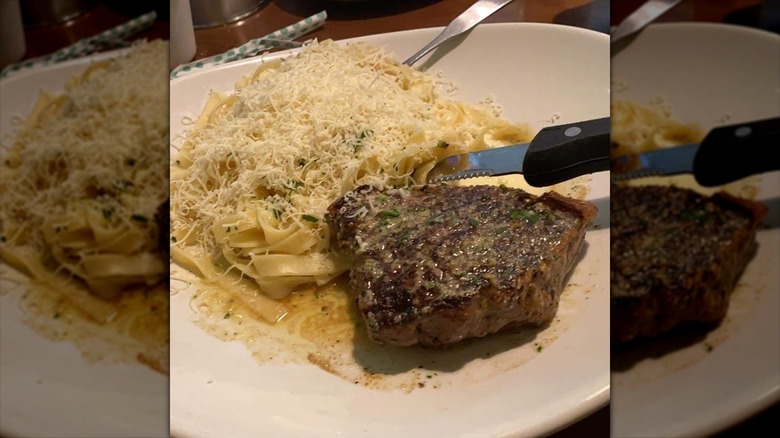 Close-up of fork and knife cutting Olive Garden alfredo and grilled sirloin