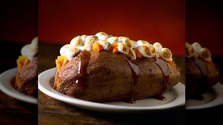 A baked sweet potato loaded with toasted marshmallows and dripping syrup on a white plate