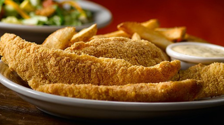 A plate with four fried catfish strips, a ramekin of tartar sauce, and steak cut fries