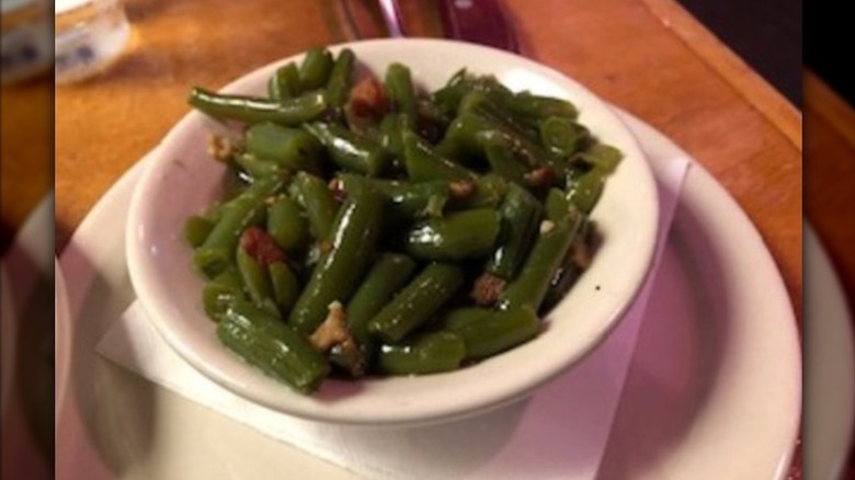A bowl of green beans garnished with bits of bacon