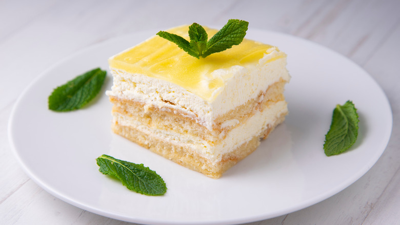 A piece of lemon tiramisu with mint leaves on a white plate