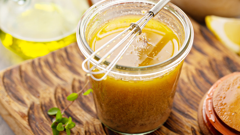 A jar full of salad dressing with a whisk on a wooden table