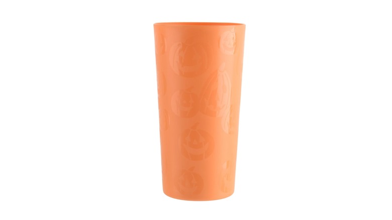 An orange tumbler with etchings of pumpkins against a white background.