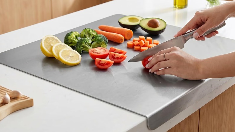 A person holding a knife to cut vegetables and fruit on a steel cutting board