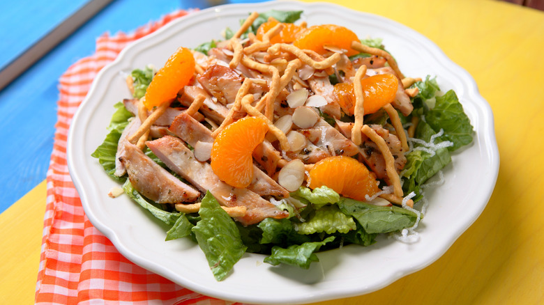 An Asian chicken salad with visible chicken breast, wonton strips, almond slivers, and mandarin oranges over romaine lettuce