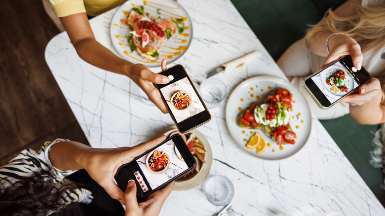 Three people at a table taking pictures of their food with cell phones