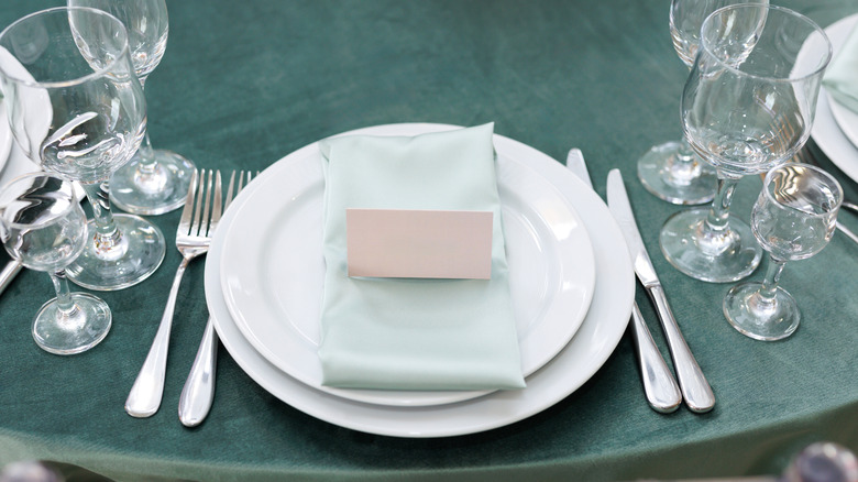 A formal table setting with two forks, two knives, multiple glasses, and a blank placard for a guest's name