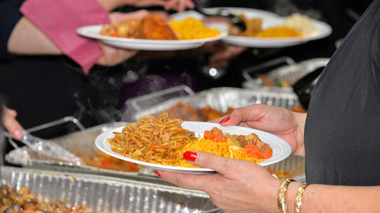 People serving themselves out of aluminum baking trays at a potluck