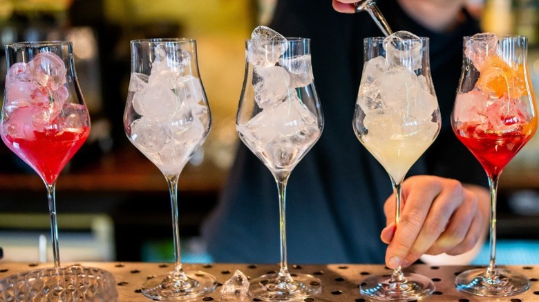 A baretender pouring liquid into stemmed glasses filled with ice