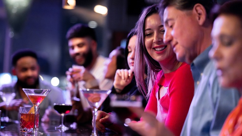 A group of people sitting at a bar with cocktails in front of them.