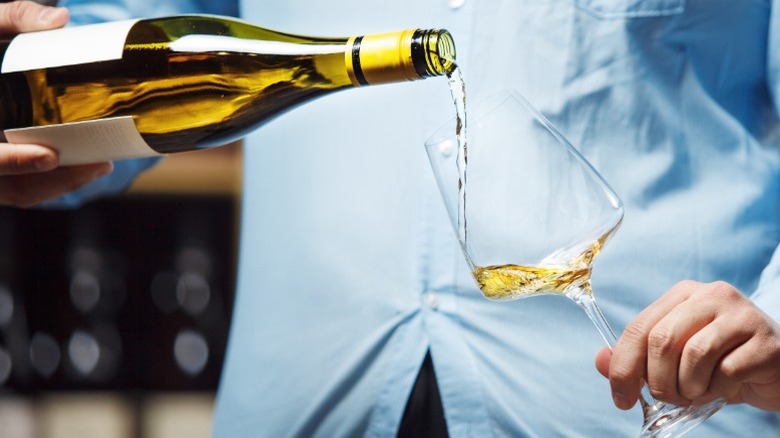 A close up of a person pouring a glass of white wine