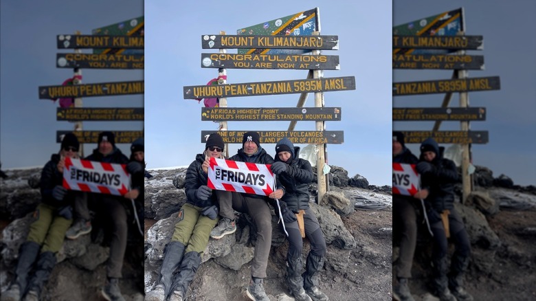 Three mountain climbers hold a TGI Fridays sign on top of Mount Kilimanjaro