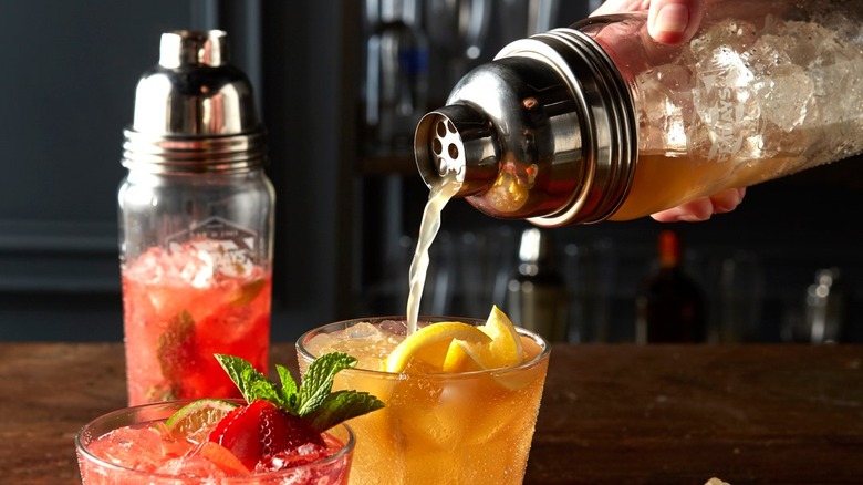 Cocktail being poured into a glass, with a second cocktail next to it and another shaker in the background
