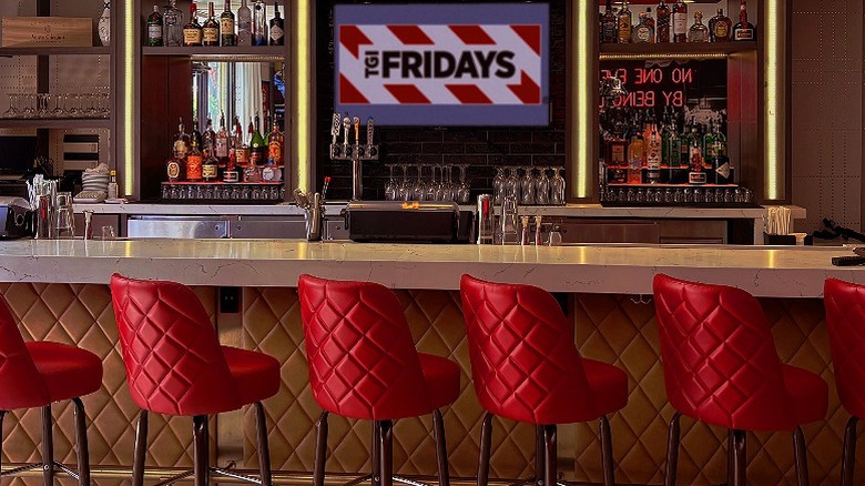 Bar area with red bar stools, bottles on the shelving and a TGI Fridays sign