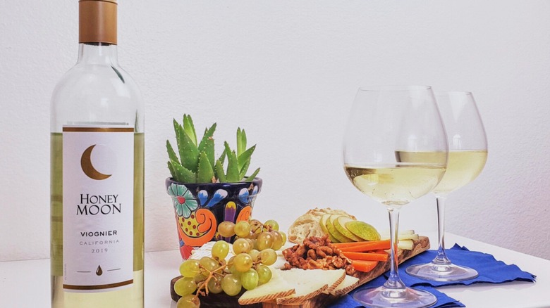 Moon wine bottle on a table with two glasses of white wine, a charcuterie board, and a succulent.