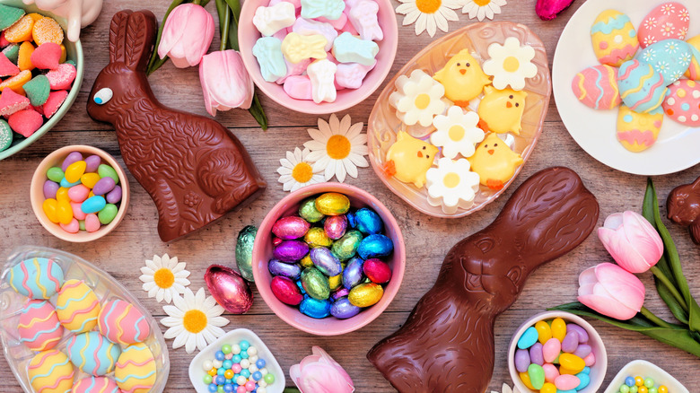 A top-down view of a table strewn with Easter bowls and plates filled and surrounded by candy, chocolates, and flowers