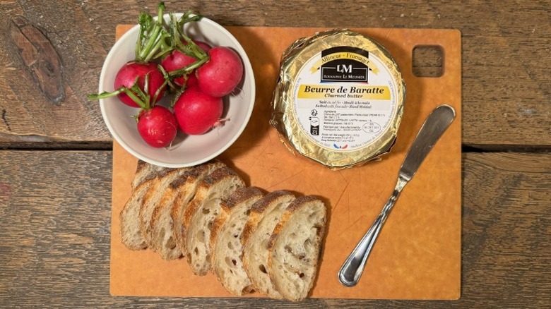 Rodolphe Le Meunier butter in its packaging on a cutting board next to a butter knife, sliced baguette, and bowl of radishes