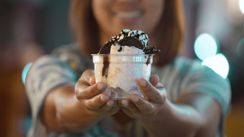Woman holding cup of ice cream with toppings