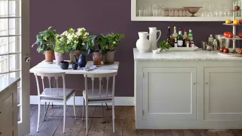 A deep purple wall in a small kitchen, with a white table and chairs and white cabinets