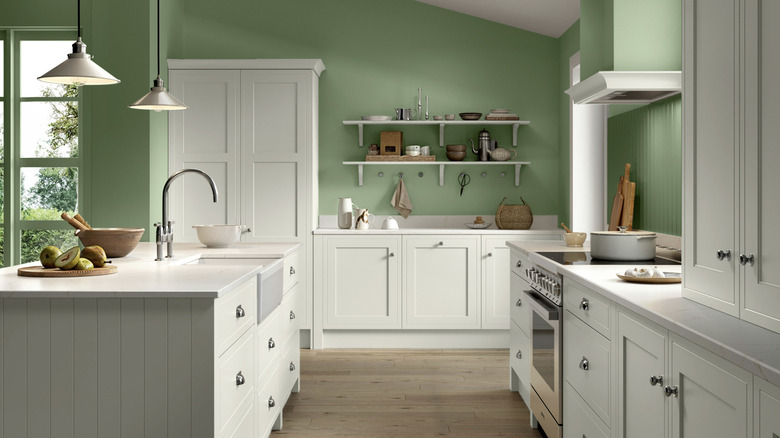 A large farmhouse kitchen with white wooden cabinets and green walls