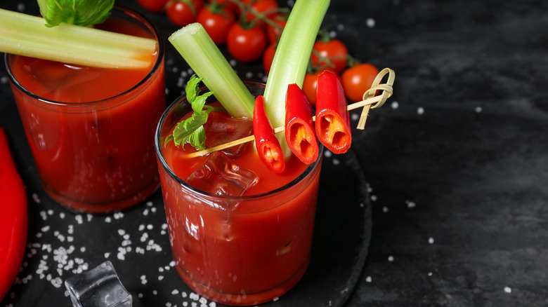 Bloody mary cocktails with red chile garnish, surrounded by salt and tomatoes