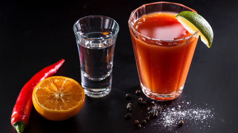 A shot of mezcal and a glass of sangrita garnished with a lime wedge, surrounded by salt, pepper, a red chile, and half an orange
